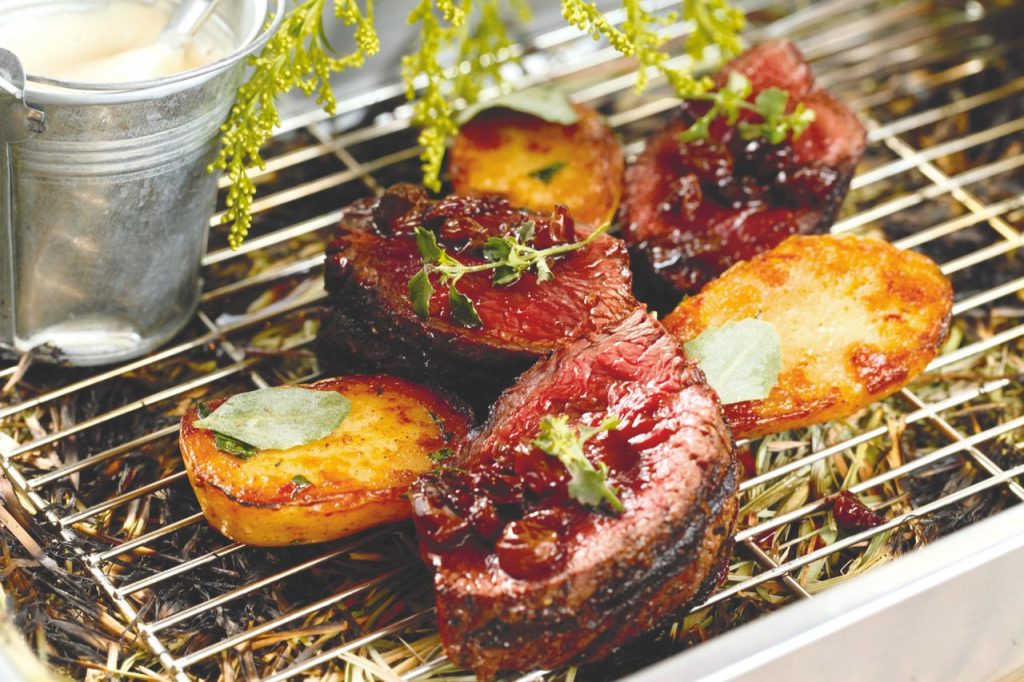 Juicy grilled steak with potatoes and herbs on a rustic barbecue grill.
